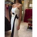 A sleek strapless black and white contrasting slit dress featuring a bold black ribbon sash tied at the waist
