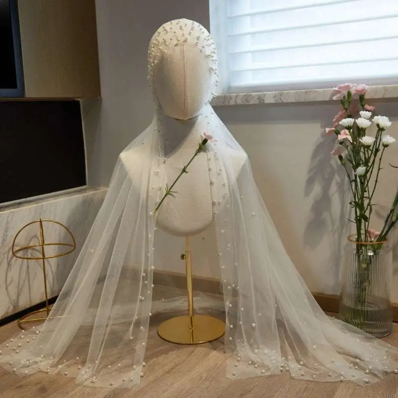 A delicate white sheer bridal hijab adorned with scattered pearls elegantly draped as a super fairy long pearl veil