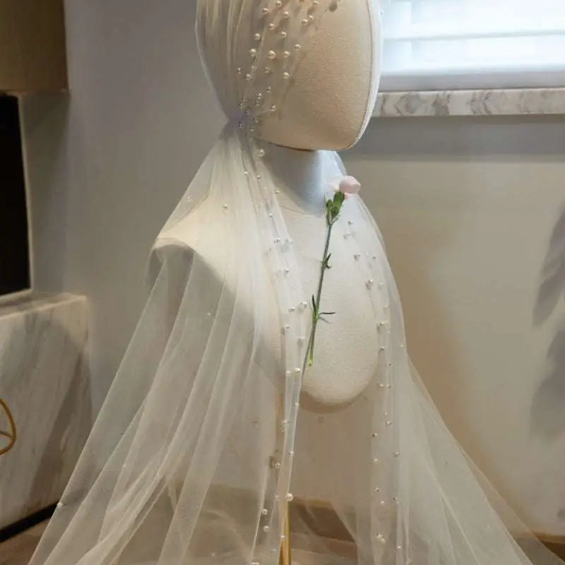 A delicate white sheer bridal hijab adorned with a fairy long pearl veil featuring small pearls along the edge