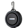 Black portable waterproof speaker with carabiner clip and perforated grille for outdoor use in luxury women’s fashion settings