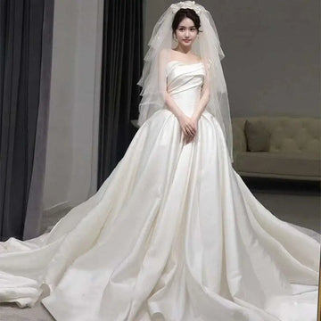 A flowing white temperament princess style french satin wedding gown with a strapless bodice and elaborate veil