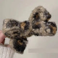 A textured winter plush bow hair clip in black beige and brown yarns with a plush leopard bow pattern