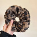 A cozy textured winter plush leopard bow hair clip with a hand-knitted brown and black curly yarn scrunchie