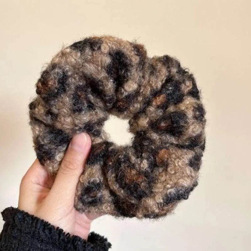 A cozy textured winter plush leopard bow hair clip with a hand-knitted brown and black curly yarn scrunchie