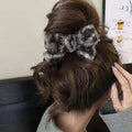 Textured winter plush bow hair clip in gray and black knitted fabric securing a brown updo hairstyle