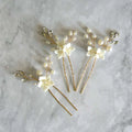 Three sets of white flower u shaped hairpins with elegant ivory flowers, clear crystals, and pearls on gold wire stems