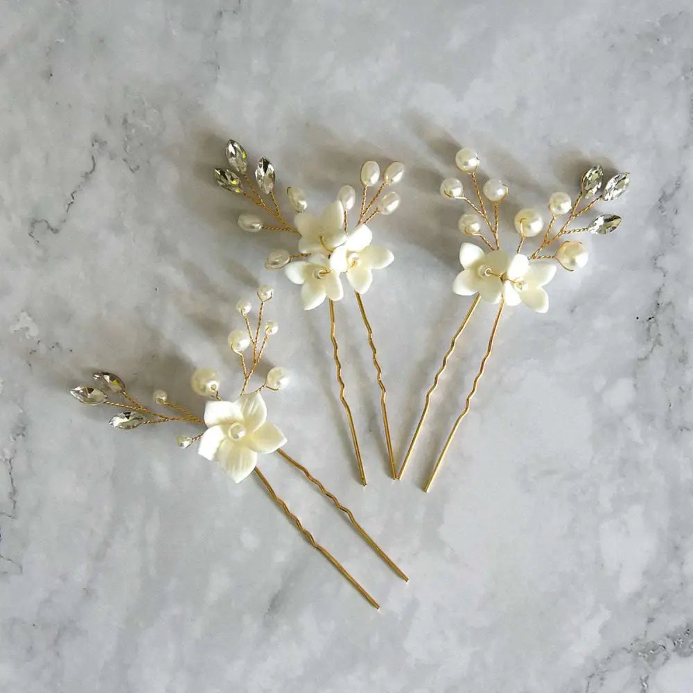 Three sets of white flower u shaped hairpins with elegant ivory flowers, clear crystals, and pearls on gold wire stems