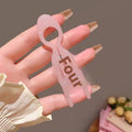 A translucent pink plastic lazy updo gadget hair clip shaped as a stylized figure with four engraved in dark brown