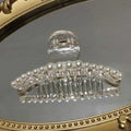 Clear acrylic pearl grab clip featuring a row of white pearls and a sparkling rhinestone bow accent