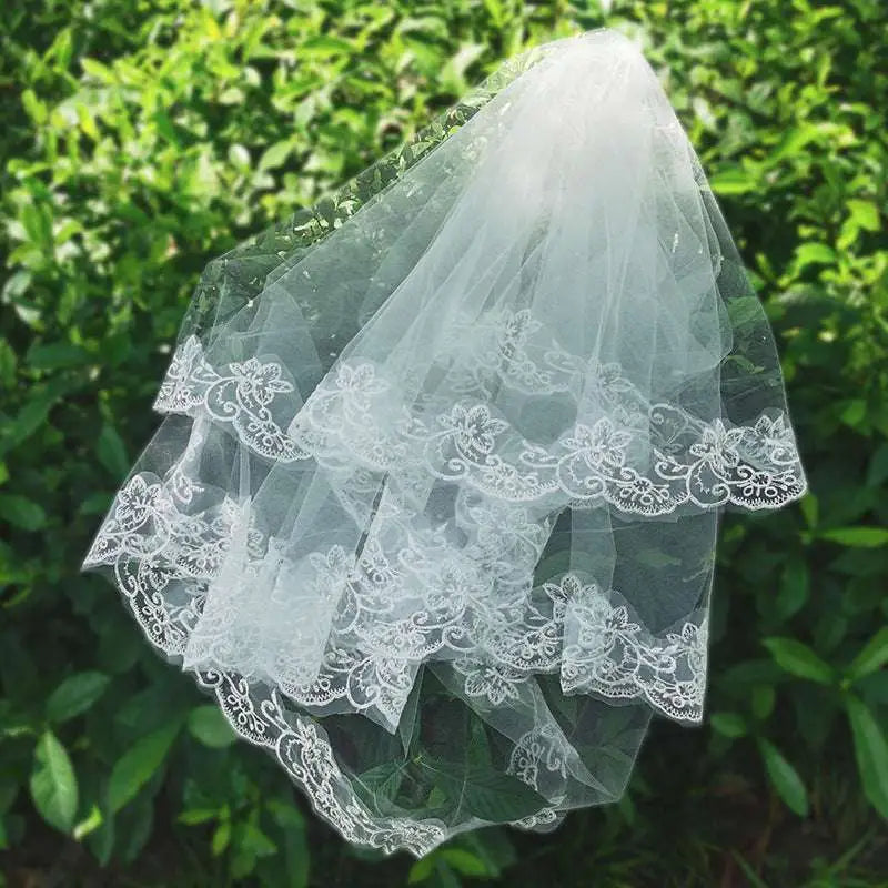 A delicate white bridal veil lace headdress featuring intricate floral embroidery and layered sheer tulle