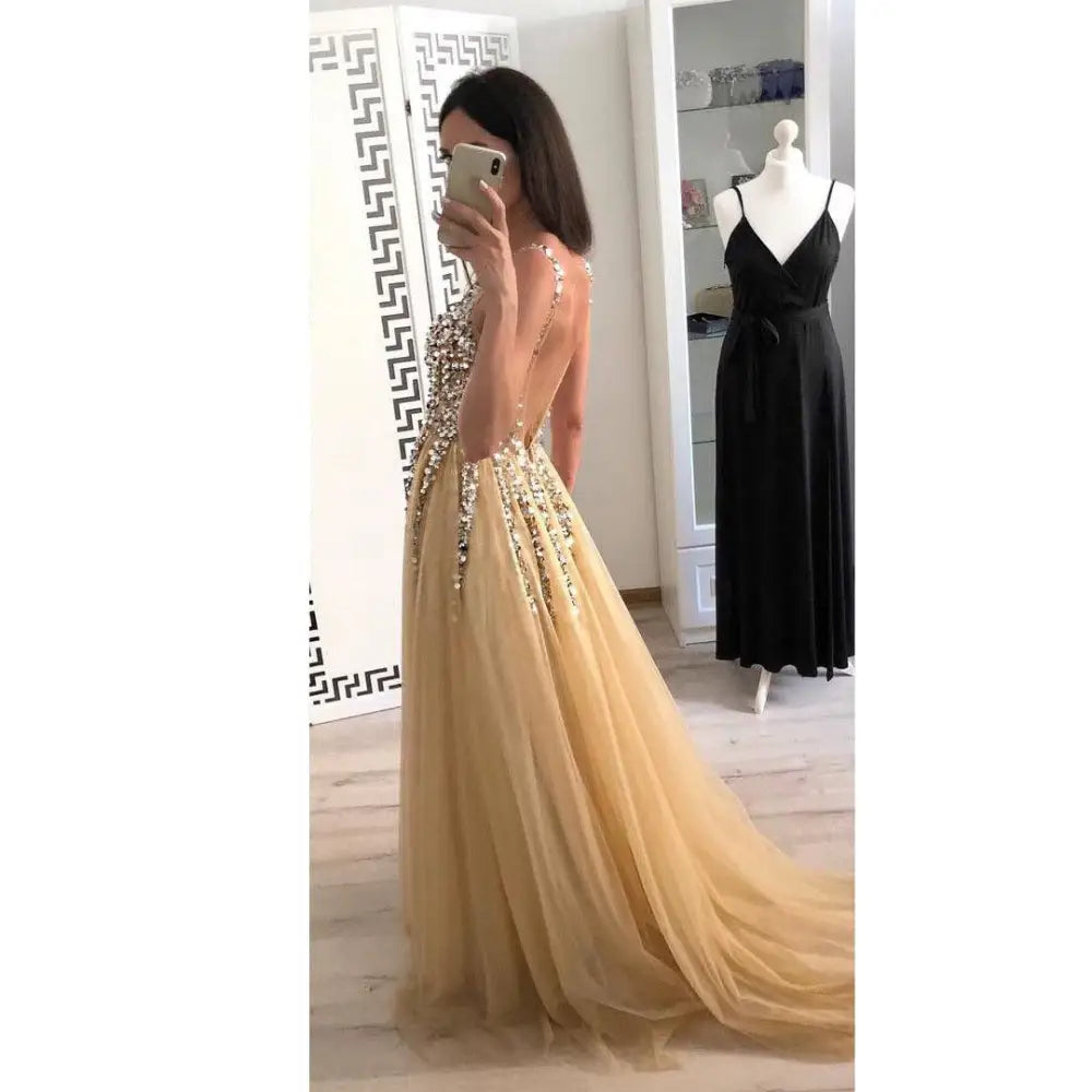 Back view of a shimmering gold v-neck sequined floor-length dress with intricate beaded embellishments and flowing tulle skirt
