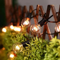 Warm waterproof string lights with clear warm-toned glass globes and black plastic bases strung along a wire