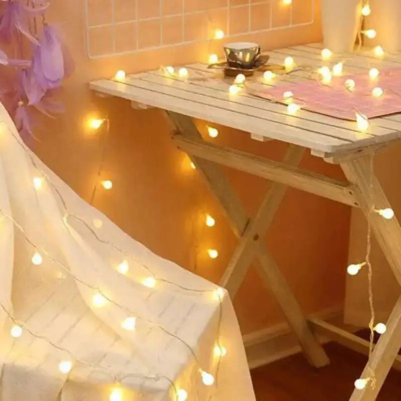 A rustic white wooden folding table with slatted top and x-shaped legs decorated with warm yellow sunshine pearl lights