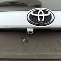 Silver toyota emblem with black perforated center on white vehicle front grille for waterproof car camera night vision reversing system