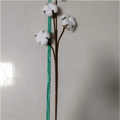 White artificial cotton stem with fluffy bolls and brown stems measured against a green tape measure