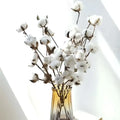 White artificial cotton stem with fluffy bolls and dark brown stalks displayed in amber glass vase with cotton flower branches