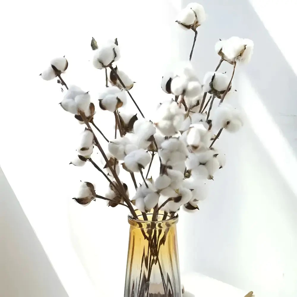 White artificial cotton stem with fluffy bolls and dark brown stalks displayed in amber glass vase with cotton flower branches