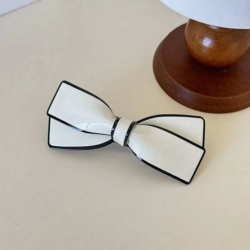 A white ceramic camellia bow spring side clip hairpin in sleek glossy resin with bold black trim for females