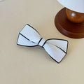 White ceramic camellia bow spring clip hairpin featuring a white bow tie with black trim and glossy finish