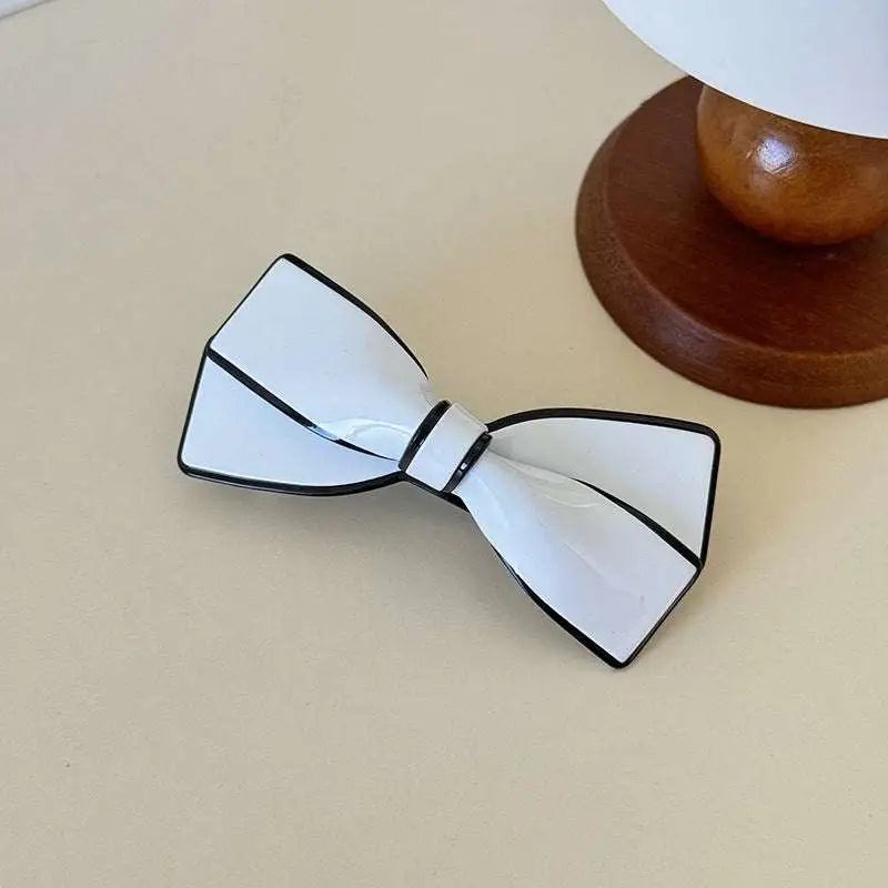 White ceramic camellia bow spring clip hairpin featuring a white bow tie with black trim and glossy finish