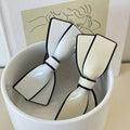 Two white ceramic camellia bow spring clip hairpins with glossy finish and black outlined edges for clip female hairpin use