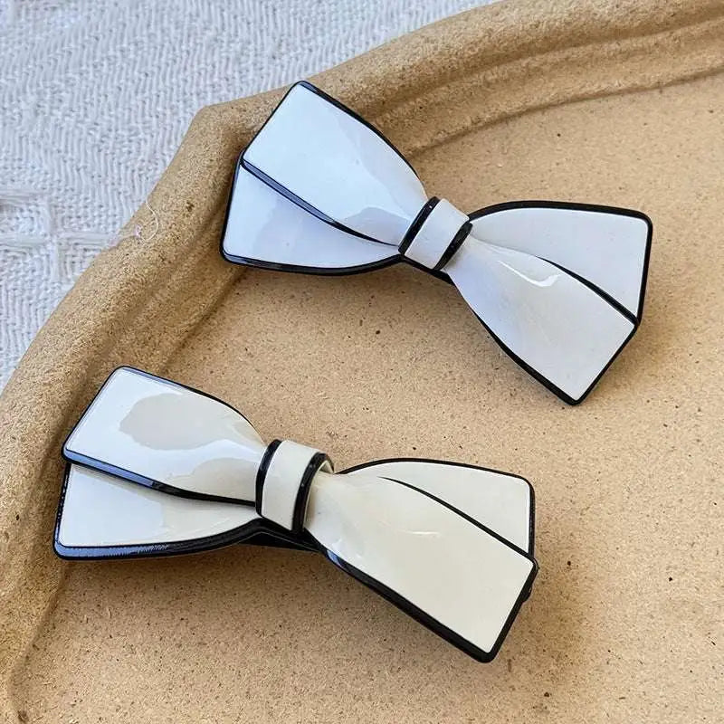 Two white ceramic camellia bow spring clip hairpins with glossy finish and black outlined edges for clip female hairpin use