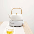 White ceramic electric earthenware oven with gold handle resting on electric kettle base showing glowing red heating