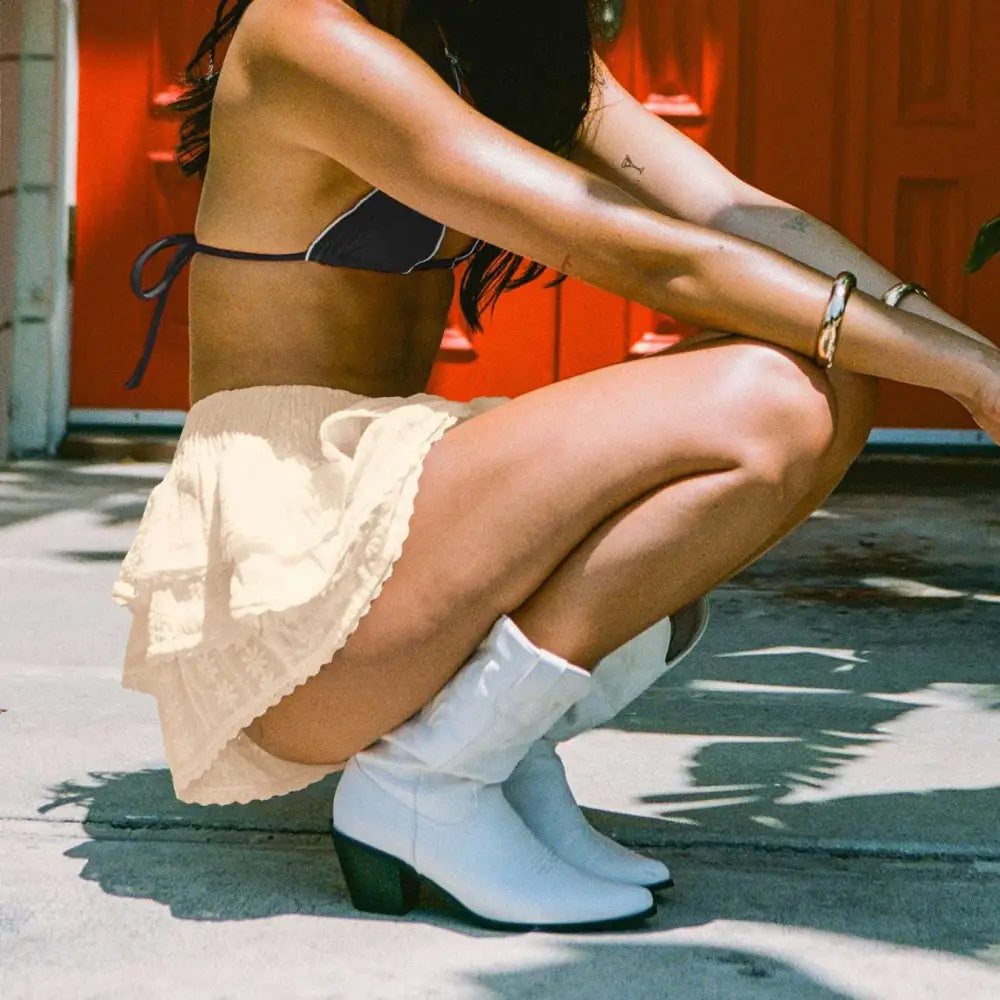 White leather cowboy boots with black heel paired with white eyelet lace bow decorative bud skirt