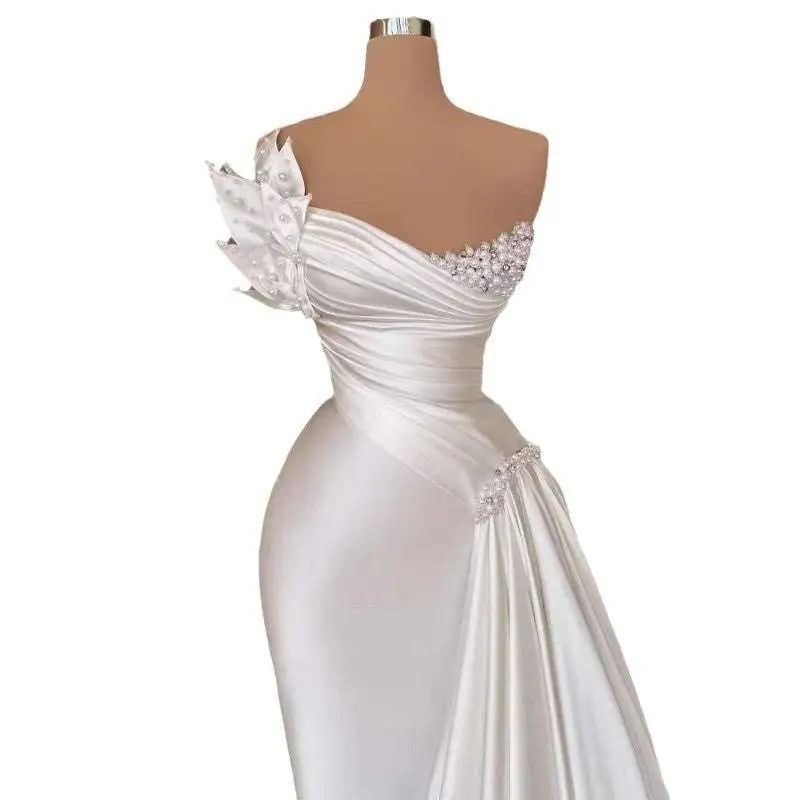 Elegant white graceful satin off-the-shoulder wedding dress with one-shoulder design, beaded embellishments, and fabric flowers