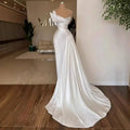 A white graceful satin off-the-shoulder wedding dress with beaded embellishments at the neckline and a flowing train