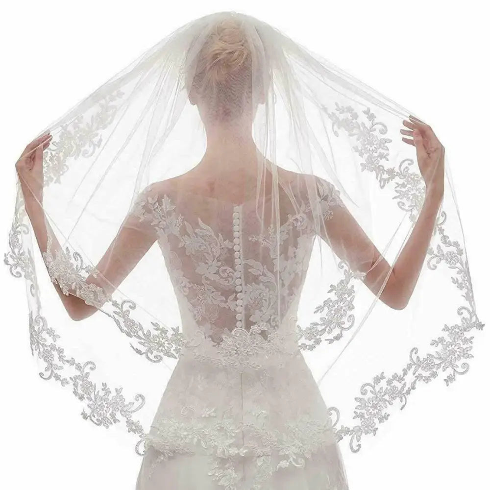 A delicate white ivory embroidery applique floral bridal veil with intricate lace edges worn by a bride