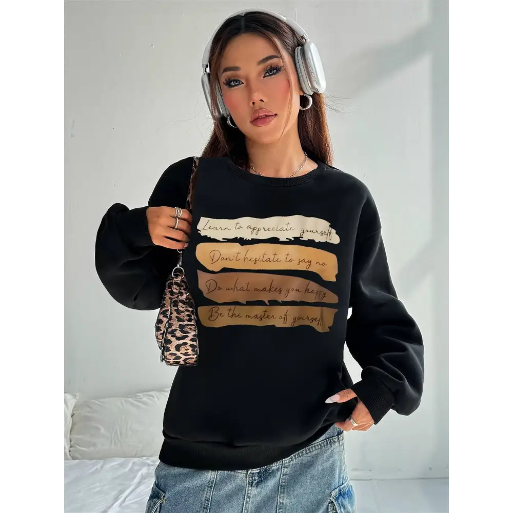 Black oversized long sleeve sweatshirt with gold-toned motivational quote printed horizontal text strips on solid colour fabric