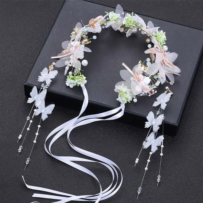Delicate white and light pink children’s wreath adorned with pearls, gold accents, butterflies, and flowing satin ribbons