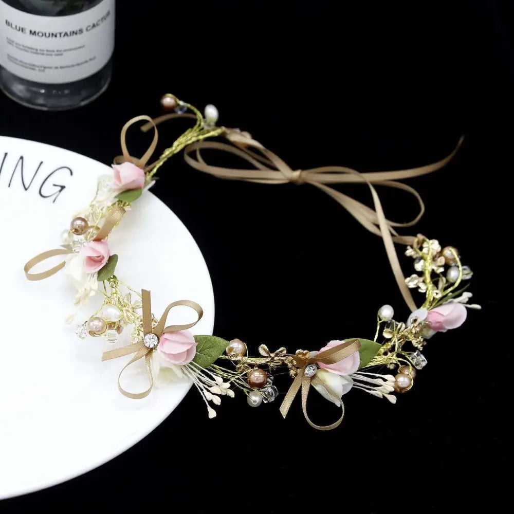 Delicate children’s wreath adorned with pink and white fabric flowers, gold stems, pearls, crystals, and beige satin ribbons