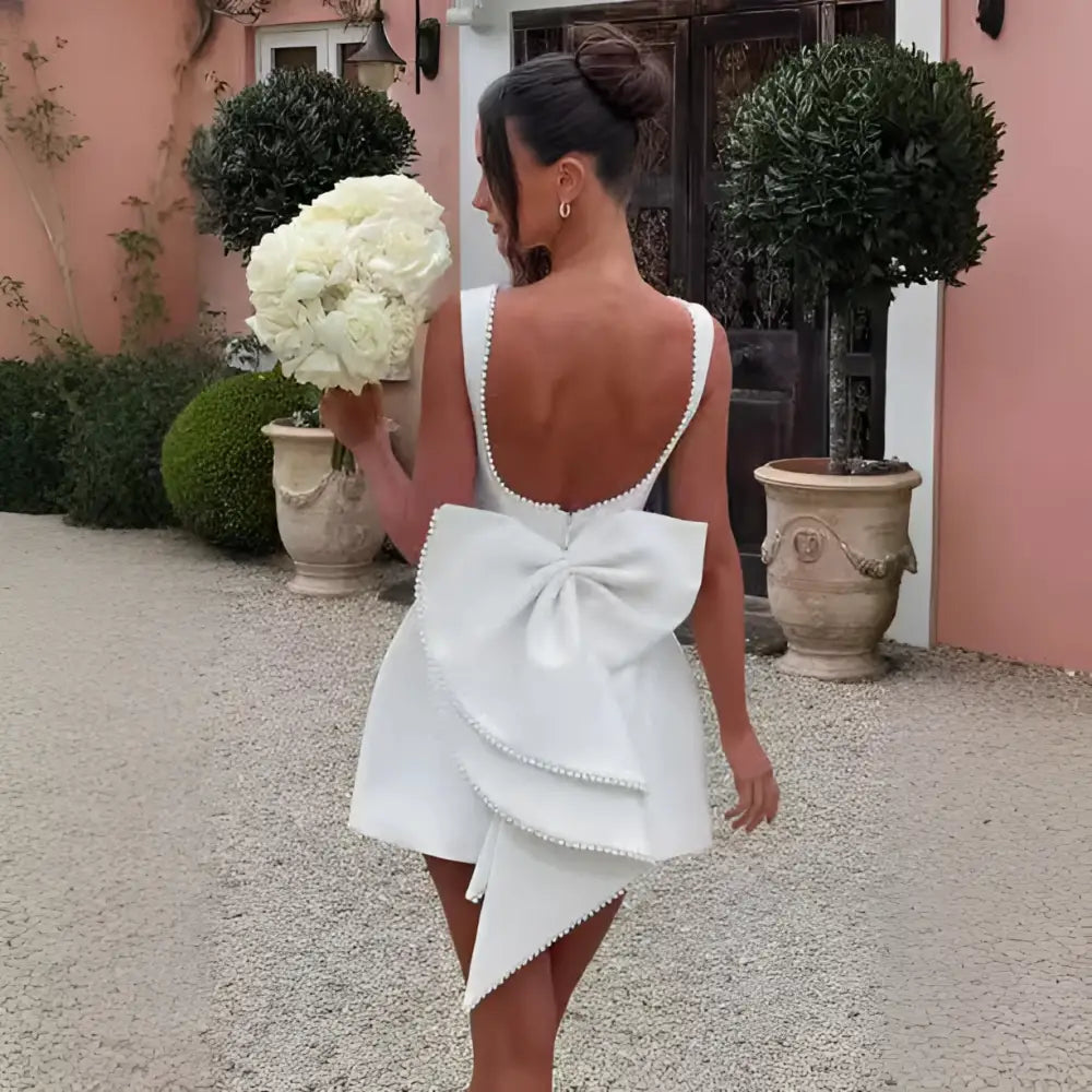 White satin backless dress summer with pearl embellished detailing, deep back cutout, and layered bow at the waist