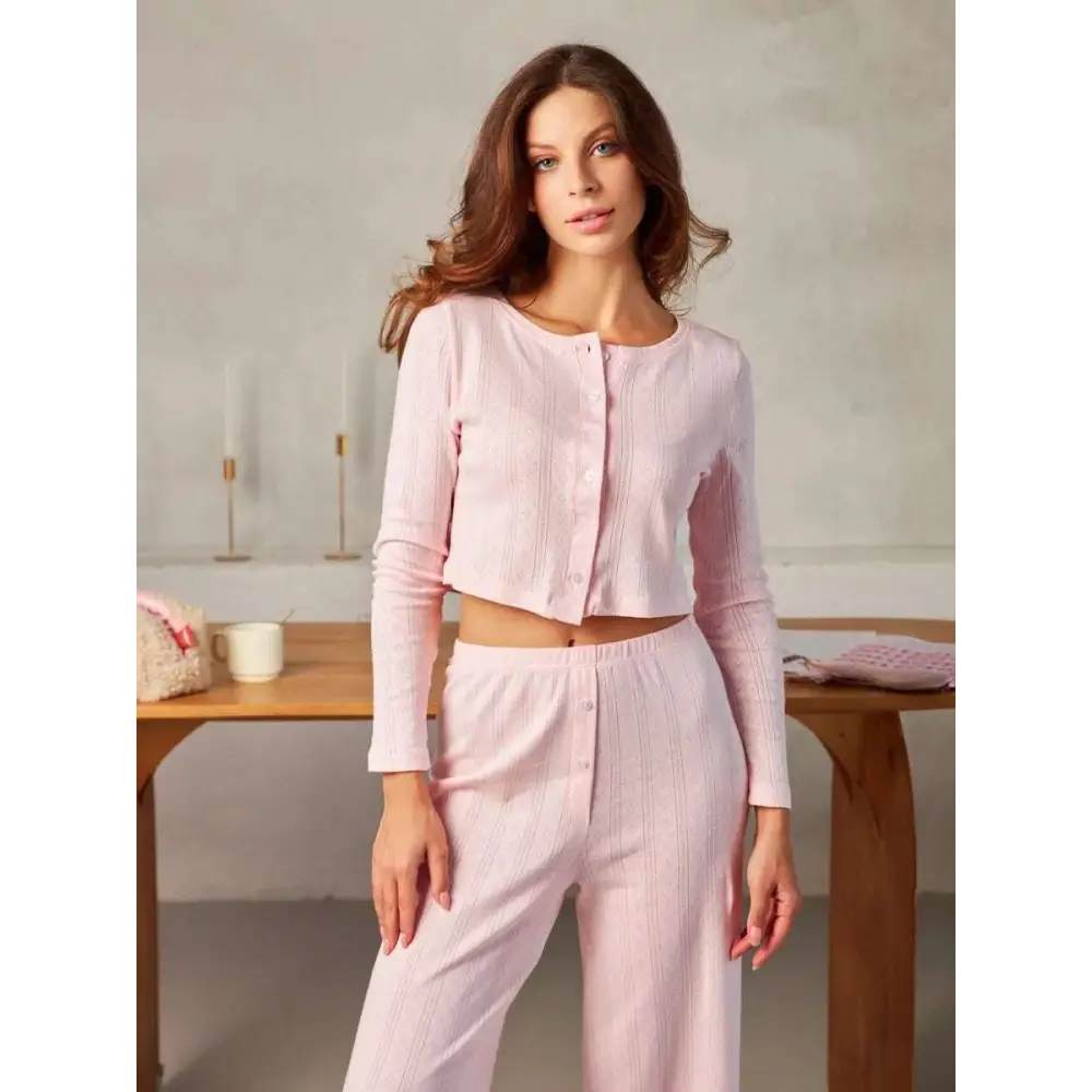 A soft pink long-sleeved button-up crop top with subtle vertical ribbing styled as a white ribbed knit fashion cardigan
