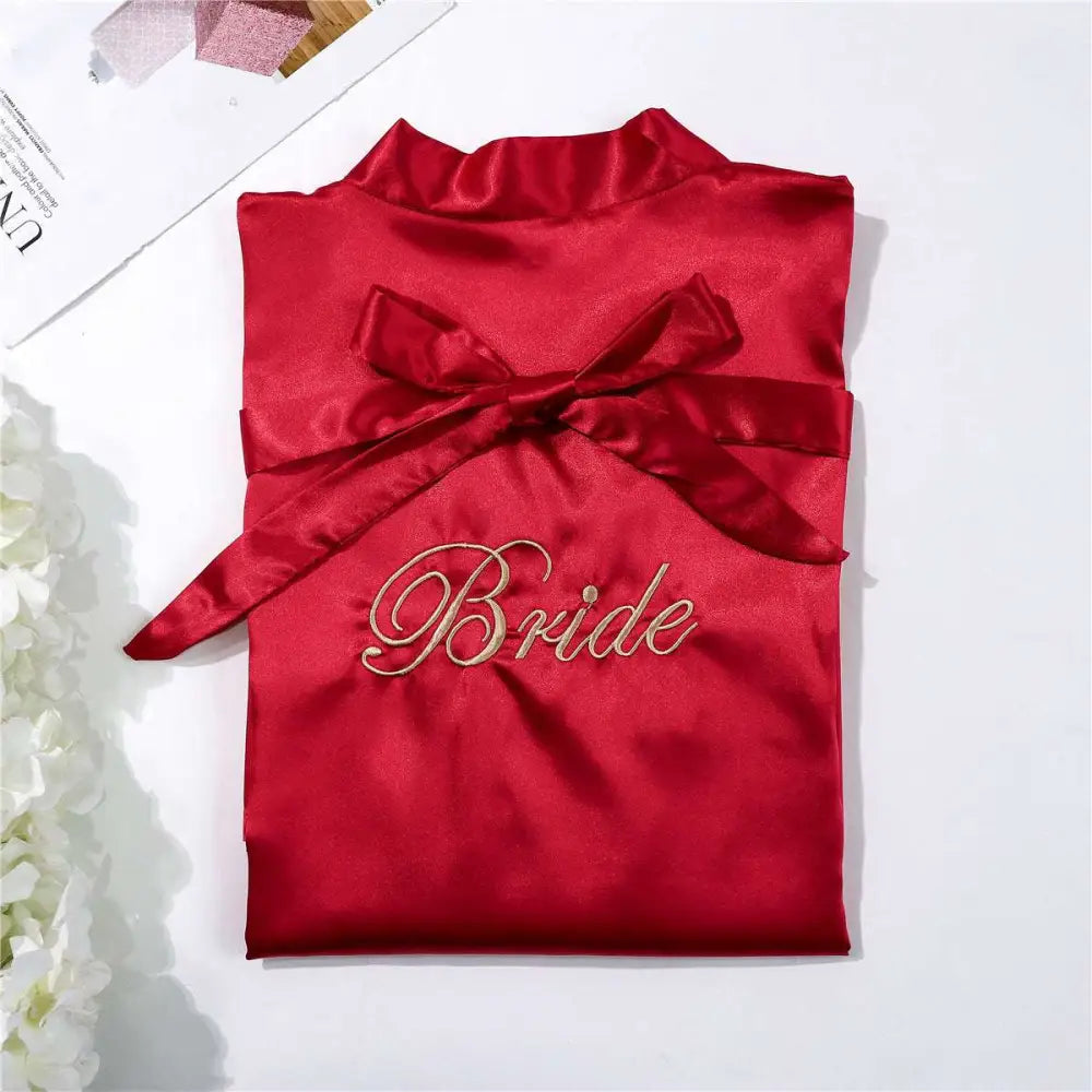 A vibrant red satin bridal pajamas simulation with gold embroidered bride script and matching waist ribbon bow