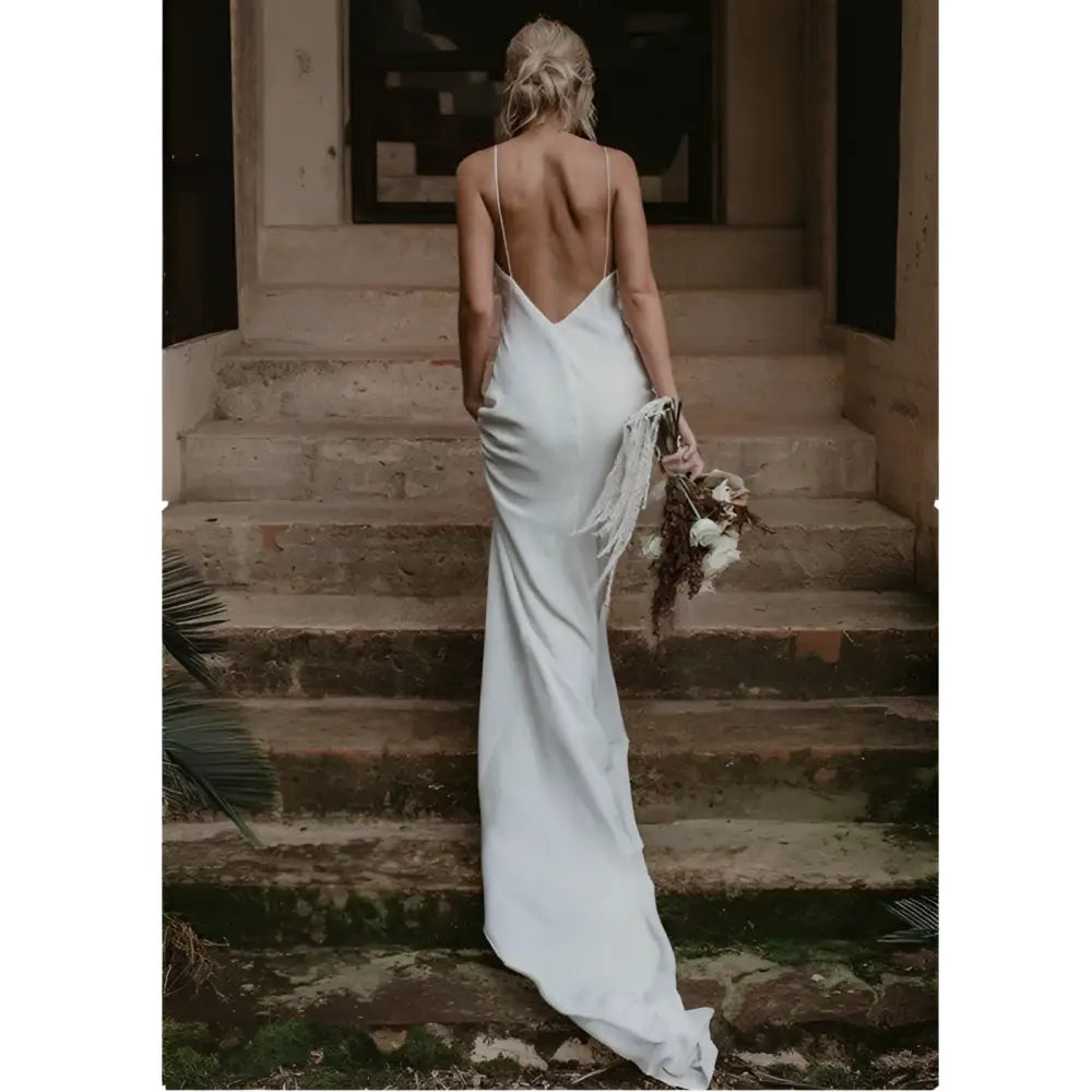 White satin evening gown with flowing train brigade and delicate spaghetti straps shown from the back side with deep cutout