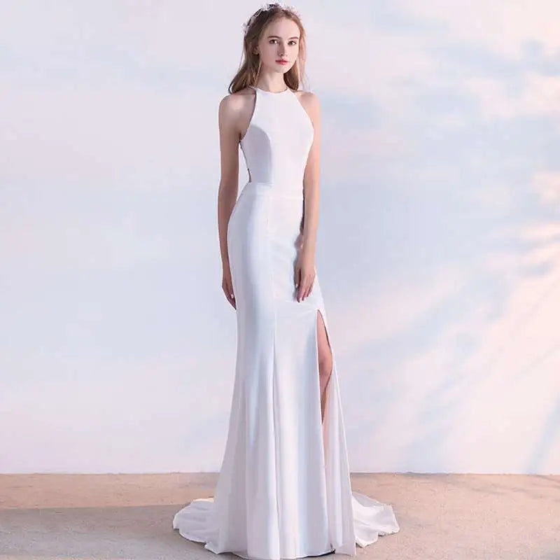 A white satin halter neck evening dress with a fitted silhouette and high slit skirt length for formal events