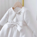 White satin long sleeve baby dress white classic style with large waist bow and rhinestone bow brooch at neckline