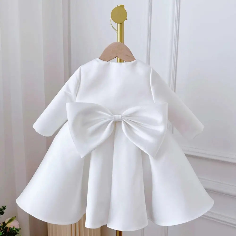 Back view of white satin long sleeve baby dress white classic style with large decorative bow on toddler dress white