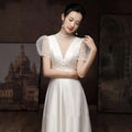 A woman wears a white satin engagement wedding dress with sheer puff sleeves and a high neckline