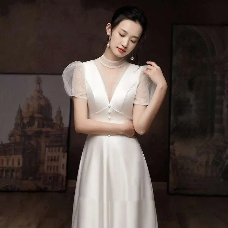 A woman wears a white satin engagement wedding dress with sheer puff sleeves and a high neckline