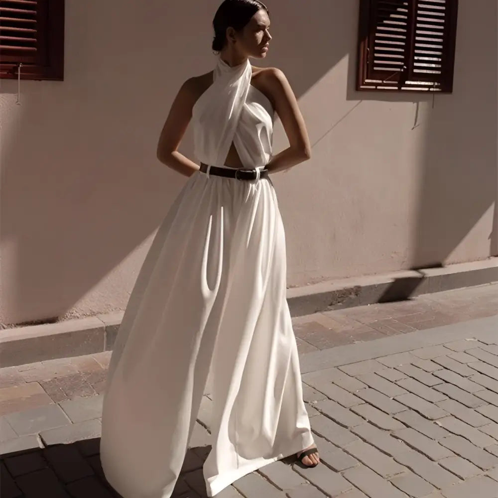 A flowing white sexy sleeveless halter backless jumpsuit with draped neckline and wide-leg silhouette cinched by black belt