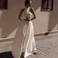 A flowing white sexy sleeveless halter backless jumpsuit with draped neckline and wide-leg silhouette cinched by black belt