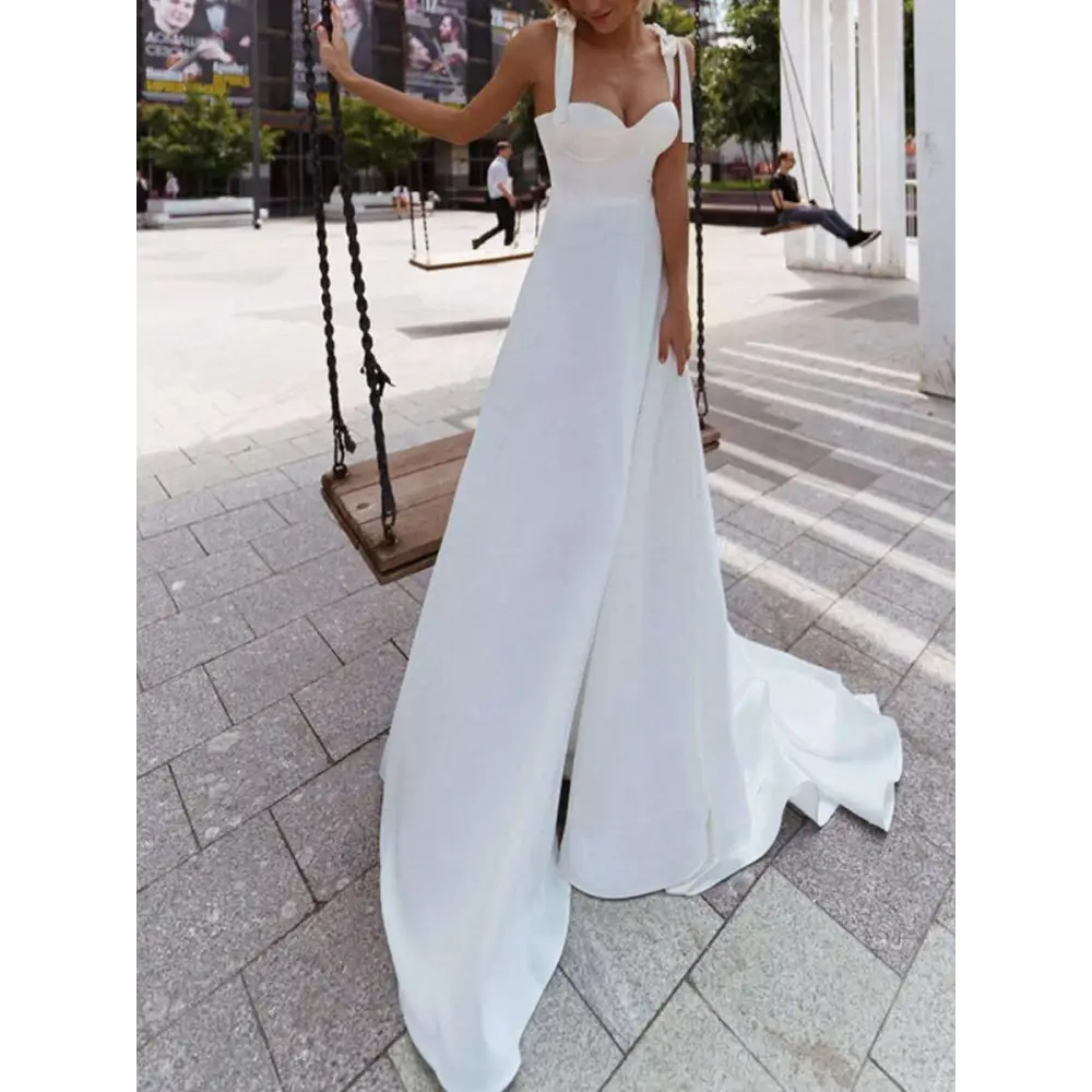 A white flowing satin wedding gown with sweetheart neckline and delicate shoulder straps featuring a sexy sling high slit