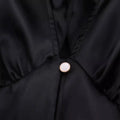 A round pearl-like button with gold rim on the black satin fabric of a white sweet satin dress with waist pleated skirt