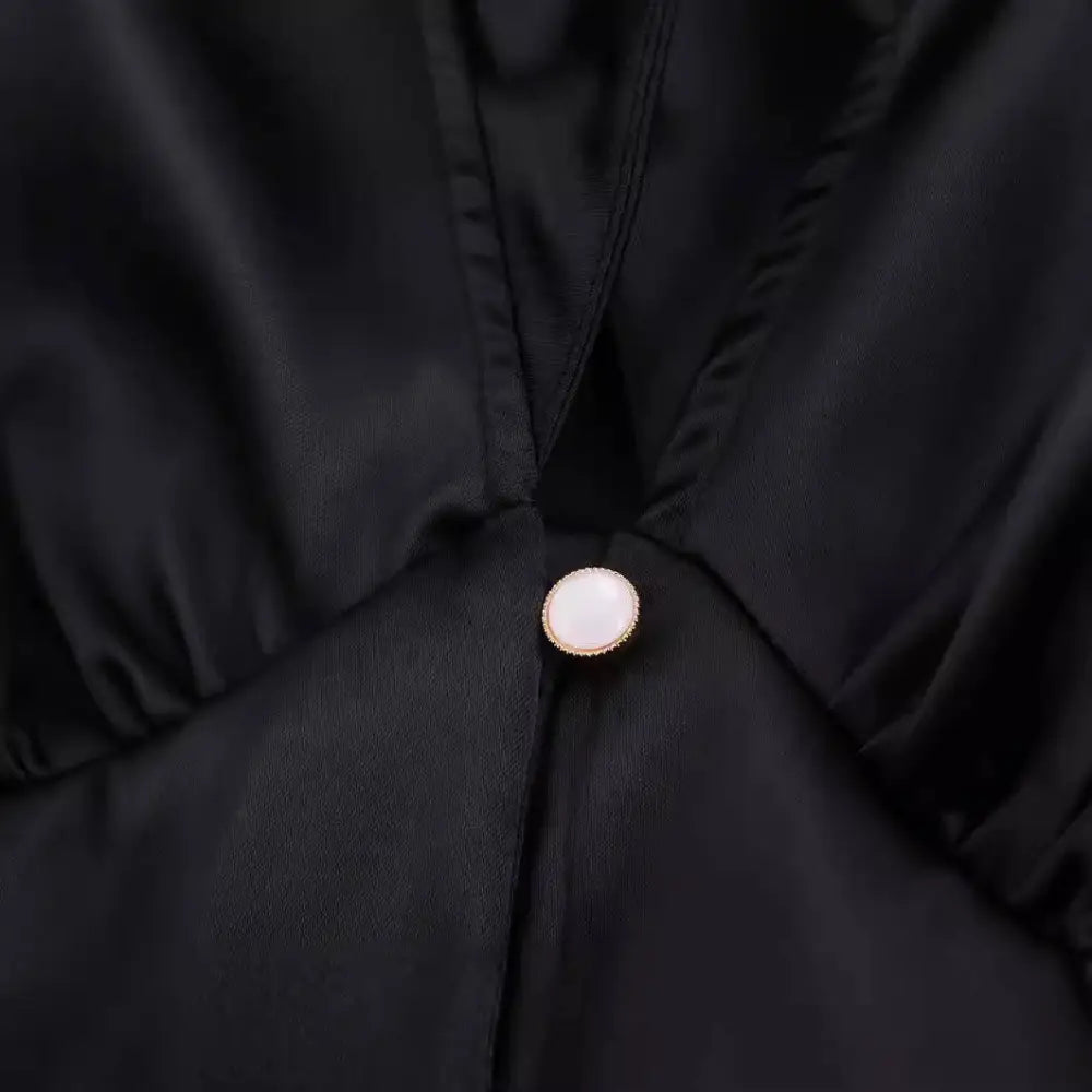 A round pearl-like button with gold rim on the black satin fabric of a white sweet satin dress with waist pleated skirt