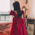 A vibrant wine red satin engagement dress with puffed sleeves, square neckline, and a large bow at the back
