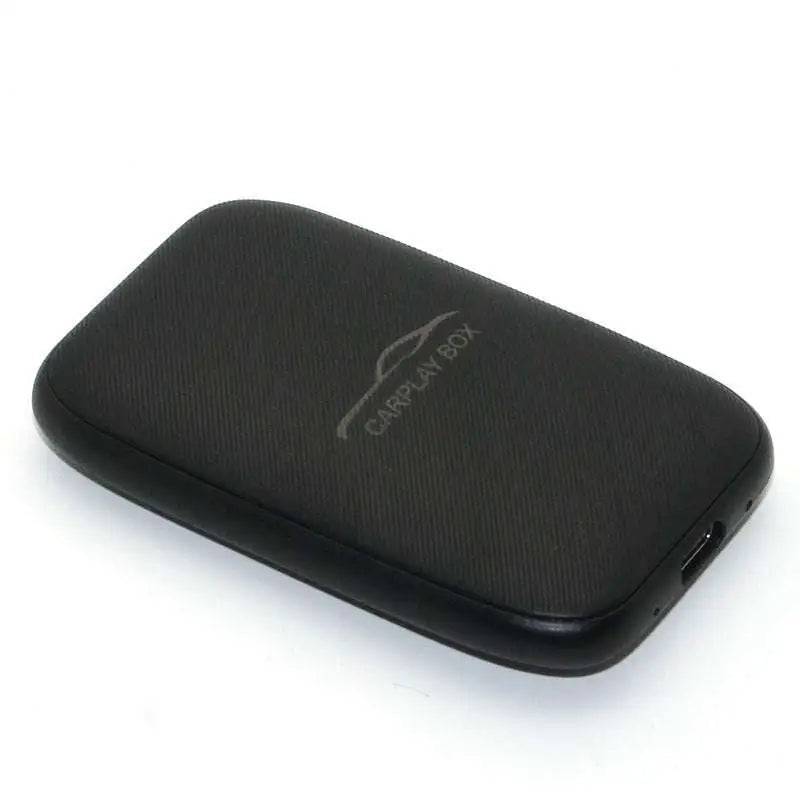Black textured rectangular wireless CarPlay box adapter with subtle silver logo and USB port for original car integration